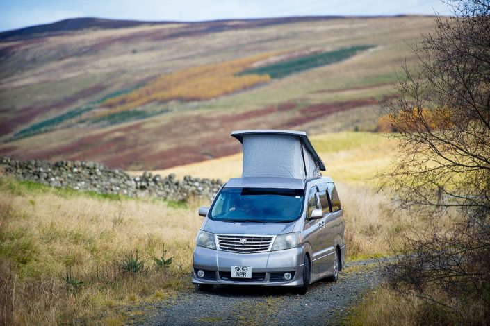 Gun Metal Toyota Alphard Hybrid Campervan with pop up roof top box on a highland pathway