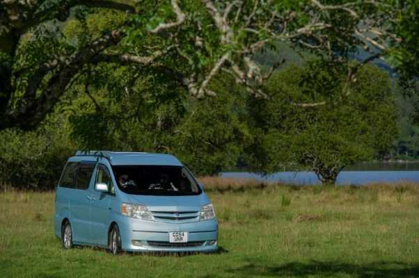 Light blue toyota alphard hybrid eco campervan for sale parked in green field