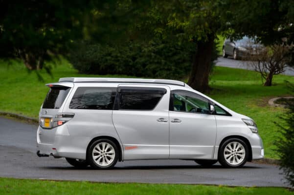 Offside view of silver Toyota Alphard Connect II Campervan in garden park with roof down