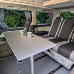 Toyota Alphard Hybrid Eco Explorer ZME white living area with table and bed up from the side